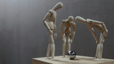 Three wooden mannequins looking at a silver ball